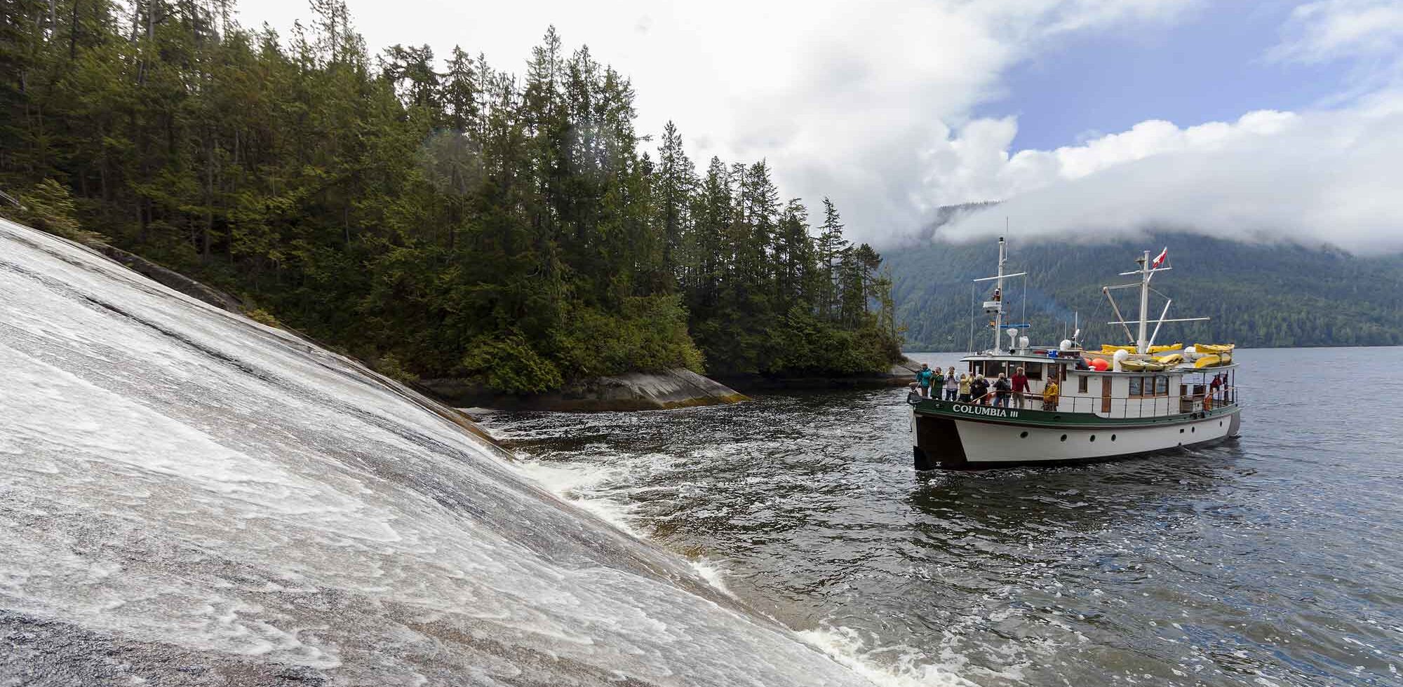The Columbia III noses into a low angle waterfall in Tribune Channel for guests to take pictures while on a photo-tour in the Broughton Archipelago. Broughton Archipelago, Central British Columbia Coast, British Columbia, Canada.