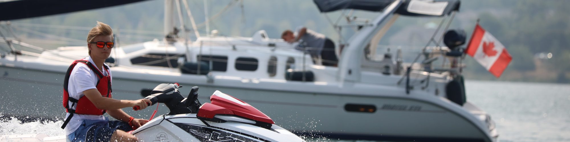 A jetskiier driving in front of a sailboat